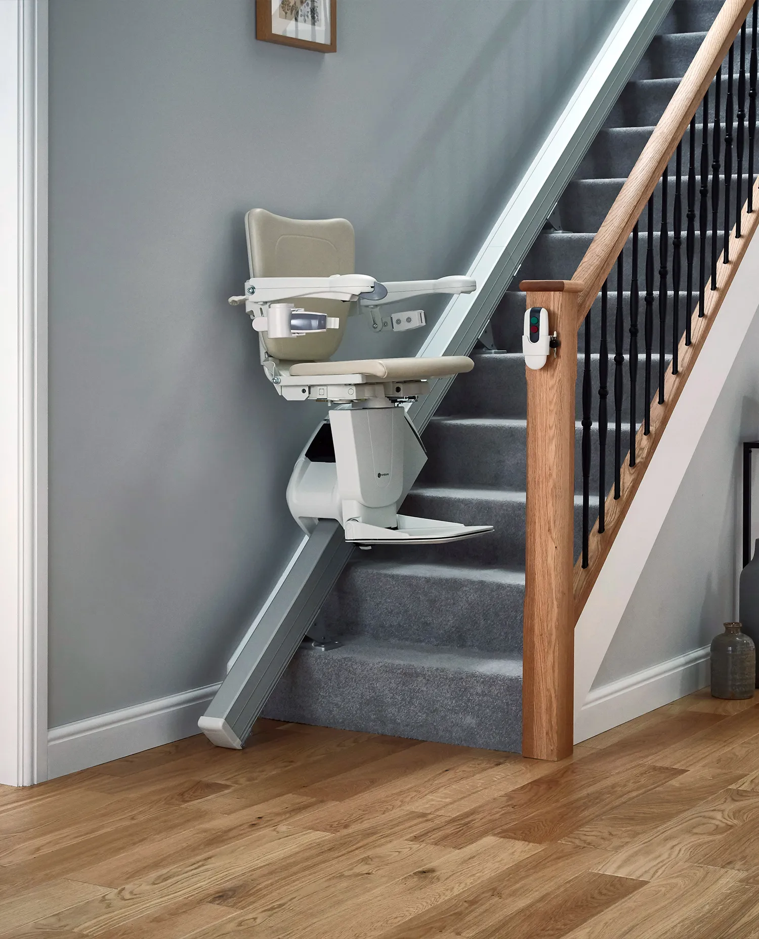 Treppenlift in Wohnhaus vor grauer Wand. Schiene führt an der Wand entlang in den ersten Stock.